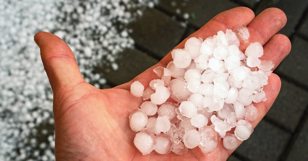 Hand holding hail on top of a roof